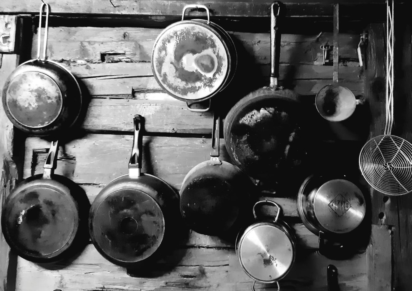 Ein Bild in Schwarzweiß: Kochgeschirr hängt an einer Holzwand.