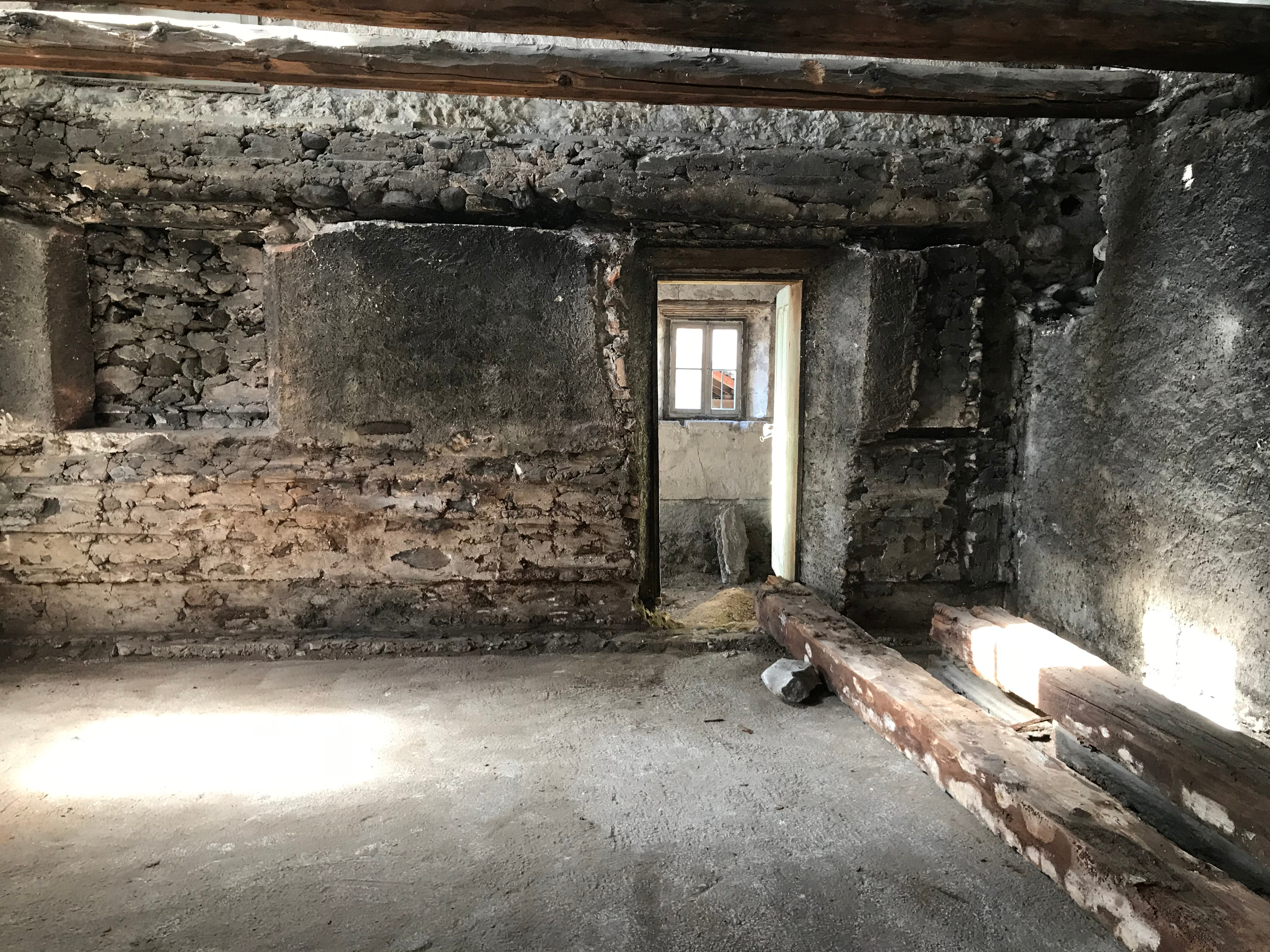 Eine offene Tür, dahinter ein teils hell zugeklebtes Fenster, rohe alte Wände, auf dem Boden liegen zwei größere unförmite Mauerstücke