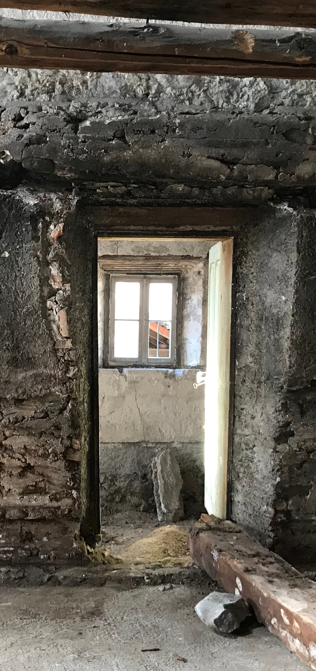 Eine offene Tür, dahinter ein teils hell zugeklebtes Fenster, rohe alte Wände, auf dem Boden liegen zwei größere unförmite Mauerstücke